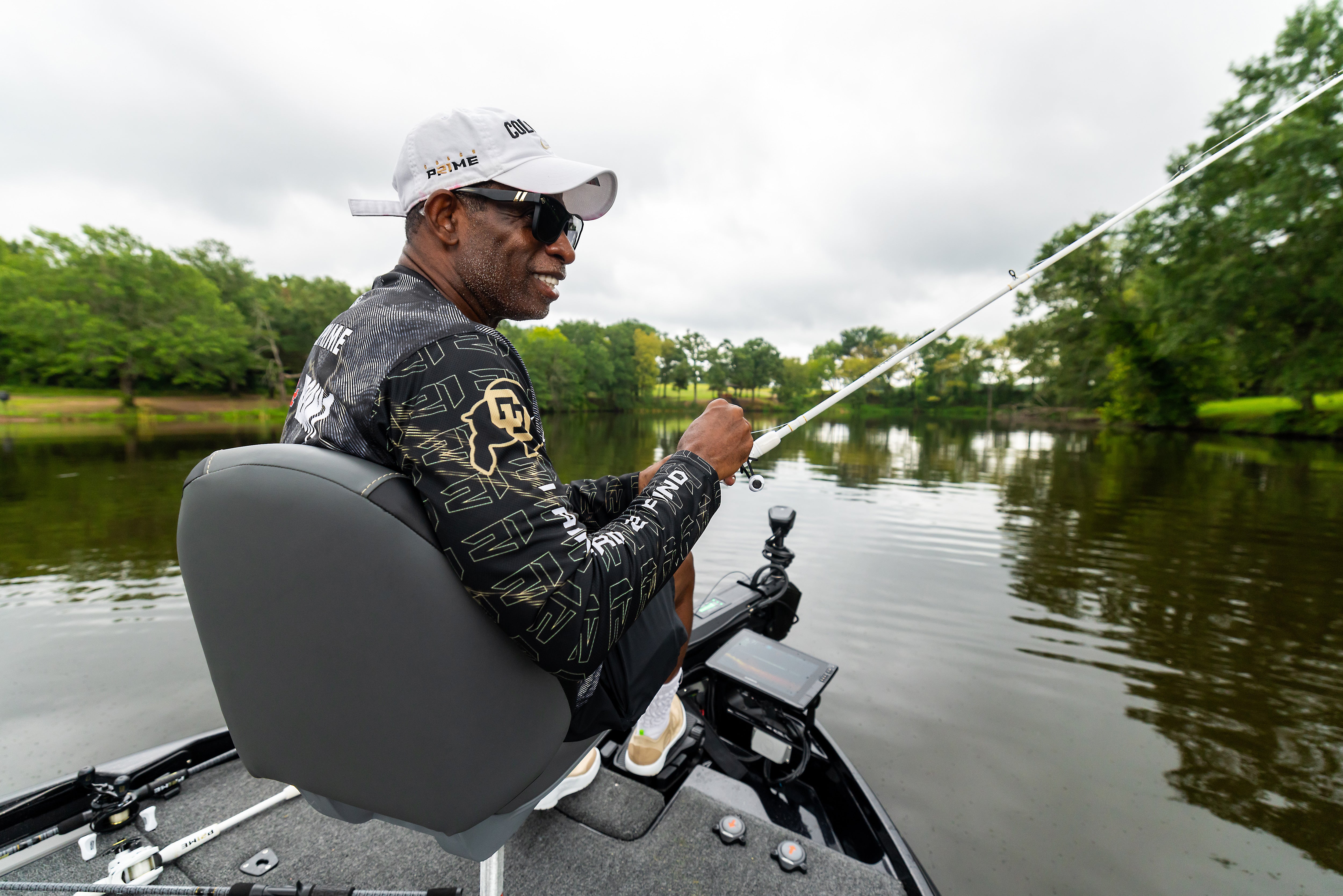 Coach Prime fishing from a boat on a calm lake with trees in the background
