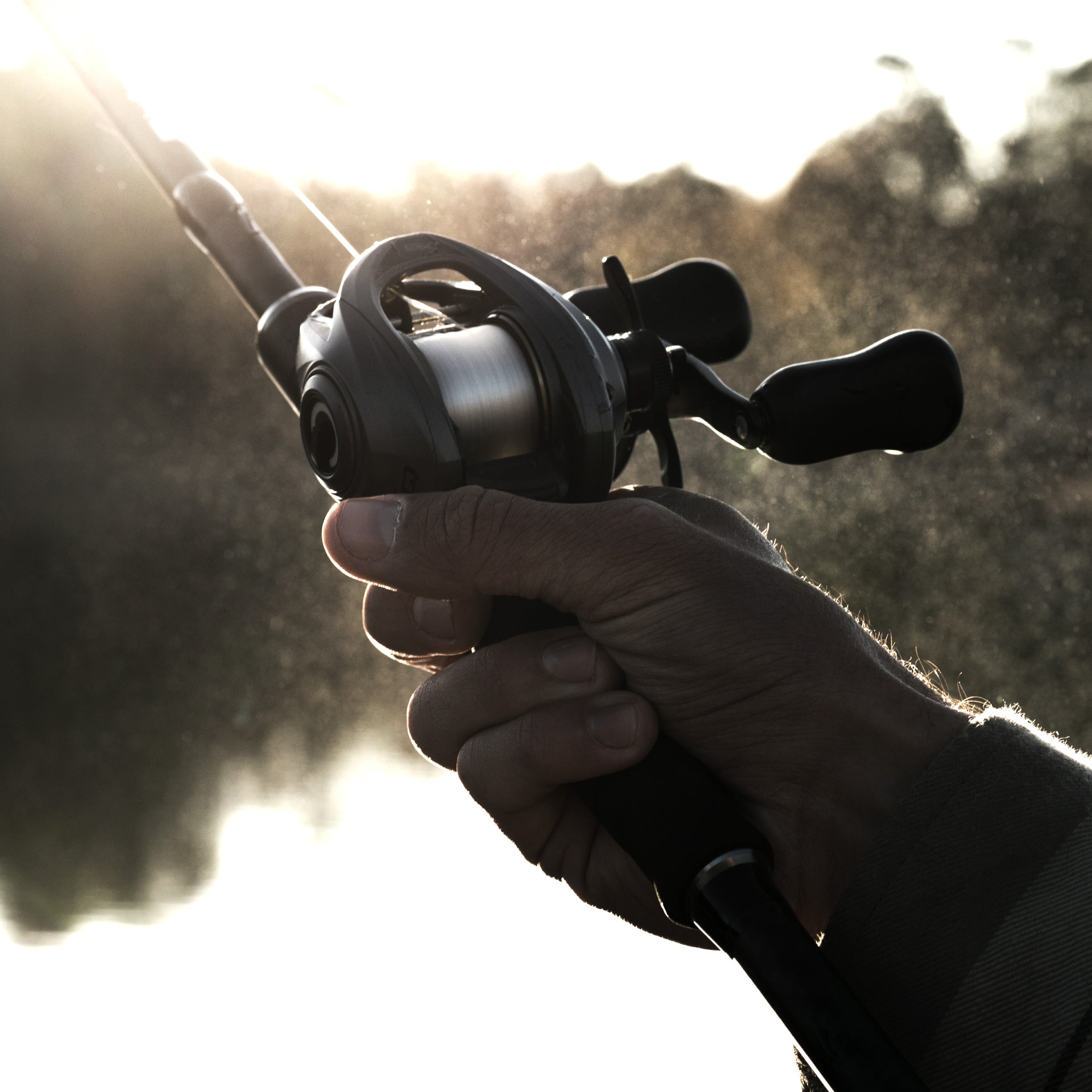 Hand holding a fishing reel with a blurred natural background