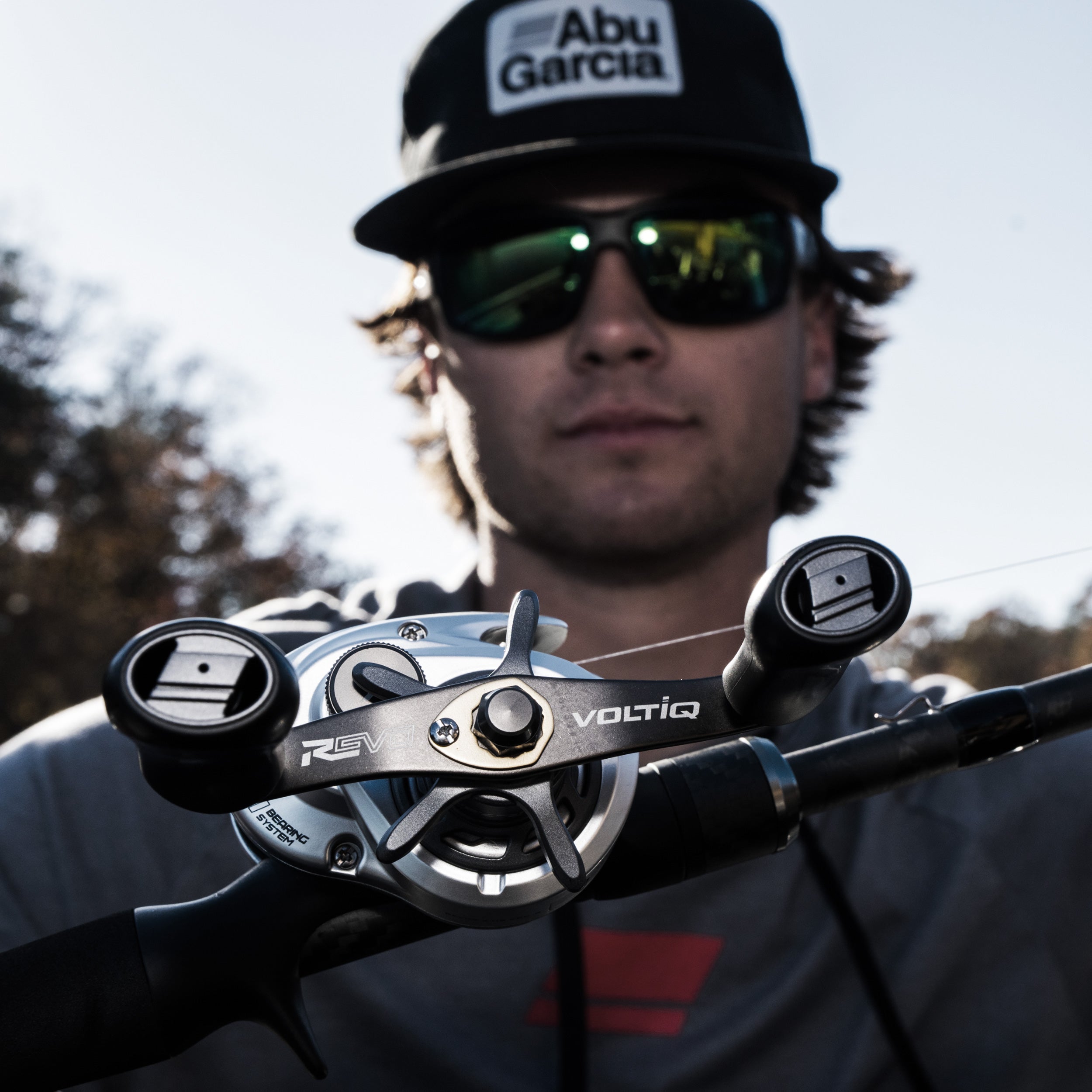 Close-up of Abu Garcia reel with person wearing sunglasses and cap in the background